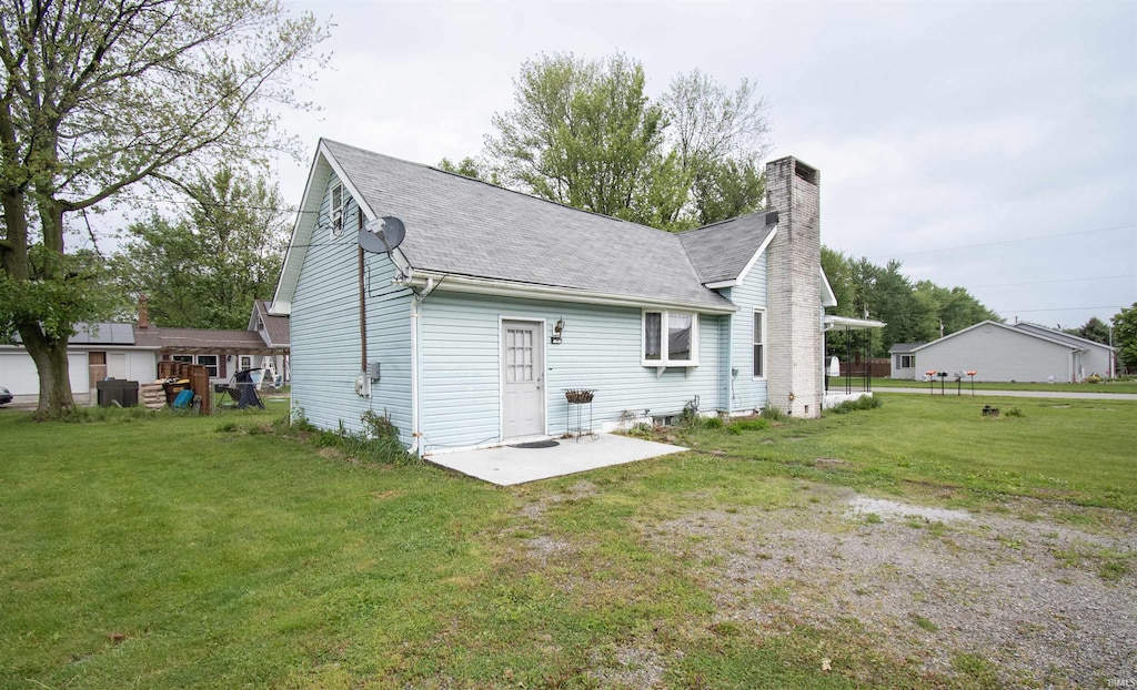 410 S Gonser Ave, Ashley, IN 46705 - back of property featuring a patio area, a shingled roof, a chimney, and a yard