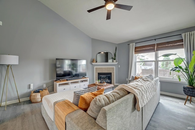 3063 N Natasha Dr, Bloomington, IN 47404 - living room with wood finished floors, ceiling fan, baseboards, a tiled fireplace, and high vaulted ceiling