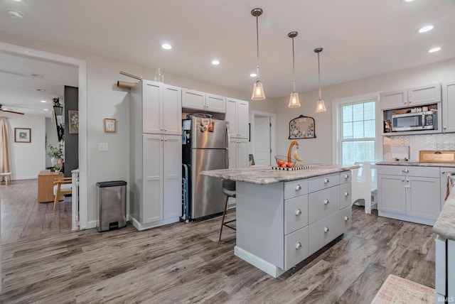 21 Noble St, Wabash, IN 46992 - kitchen featuring appliances with stainless steel finishes, a kitchen island, light wood-style flooring, tasteful backsplash, and decorative light fixtures