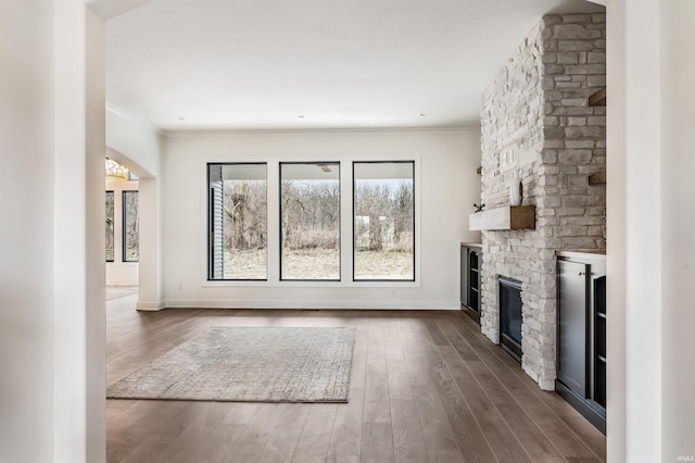 12318 Rain Lily Ct, Fort Wayne, IN 46814 - unfurnished living room with a stone fireplace, crown molding, dark wood-style flooring, and baseboards