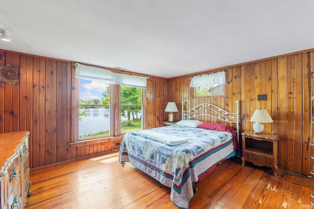 9465 E 1000 N, Syracuse, IN 46567 - bedroom featuring light wood-style floors, a textured ceiling, a water view, and wooden walls