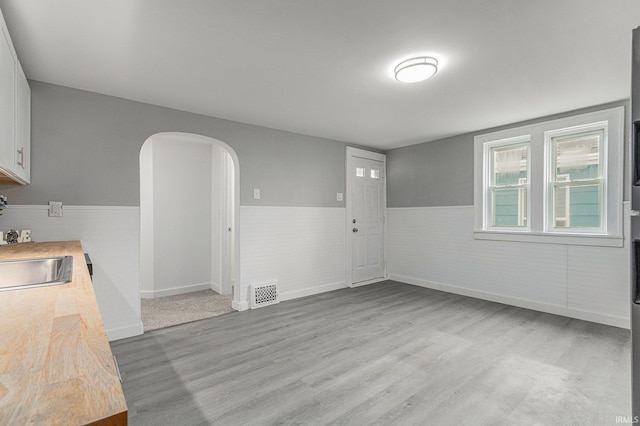 420 W 10th St, Mishawaka, IN 46544 - unfurnished dining area with a wainscoted wall, light wood finished floors, arched walkways, and a sink