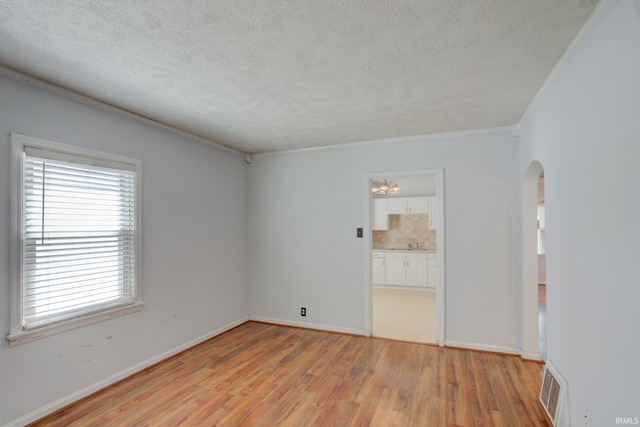 1521 Monroe Ave, Evansville, IN 47714 - empty room featuring arched walkways, light wood-style floors, a textured ceiling, crown molding, and baseboards