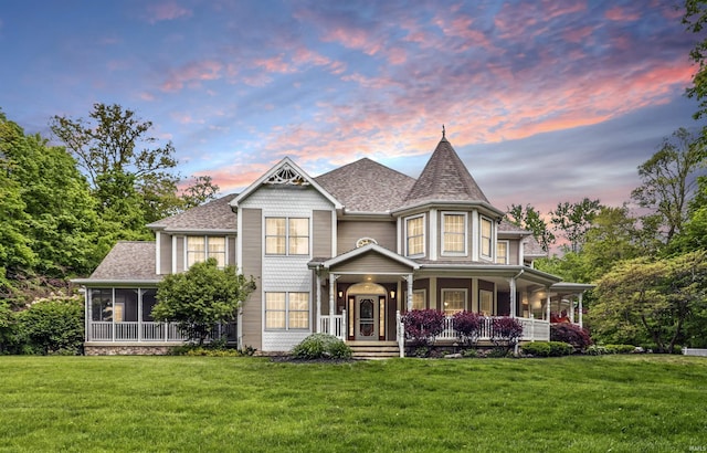 victorian-style house with a front lawn, a porch, roof with shingles, and a sunroom