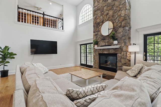 living room featuring a high ceiling, a fireplace, baseboards, wood finished floors, and healthy amount of natural light