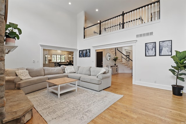 living area featuring a towering ceiling, stairway, wood finished floors, baseboards, and recessed lighting
