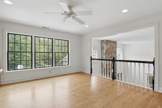 empty room with plenty of natural light, wood finished floors, a ceiling fan, recessed lighting, and baseboards