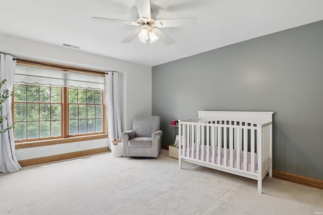 carpeted bedroom featuring baseboards, a crib, and ceiling fan