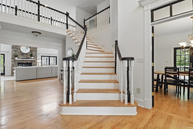 stairway with a towering ceiling, a chandelier, wood finished floors, baseboards, and a stone fireplace