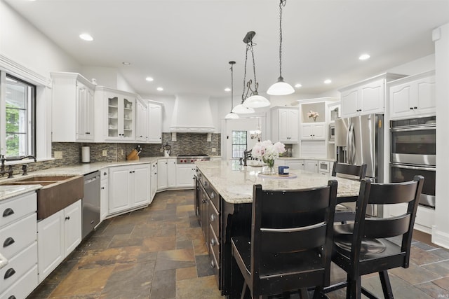 kitchen featuring custom range hood, appliances with stainless steel finishes, stone tile flooring, white cabinetry, and recessed lighting