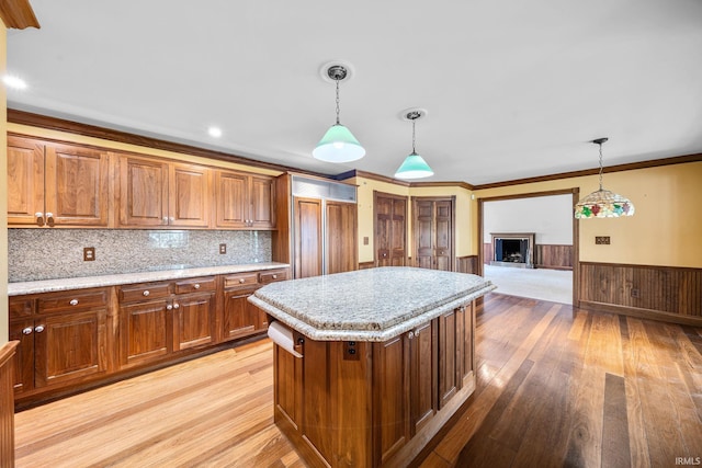 3619 Sullivan Ct, South Bend, IN 46614 - kitchen with light wood-style flooring, brown cabinets, wainscoting, hanging light fixtures, and a kitchen island