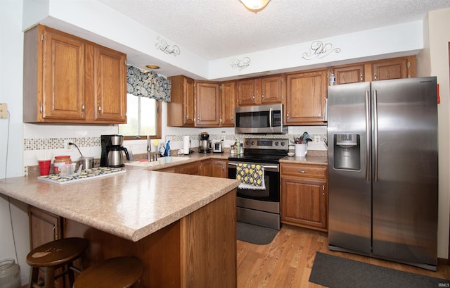 1220 N 290, Angola, IN 46703 - kitchen with appliances with stainless steel finishes, a peninsula, brown cabinets, a sink, and a textured ceiling