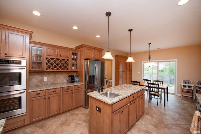 6118 Mackenzie Ct, West Lafayette, IN 47906 - kitchen featuring appliances with stainless steel finishes, a sink, brown cabinetry, an island with sink, and decorative backsplash