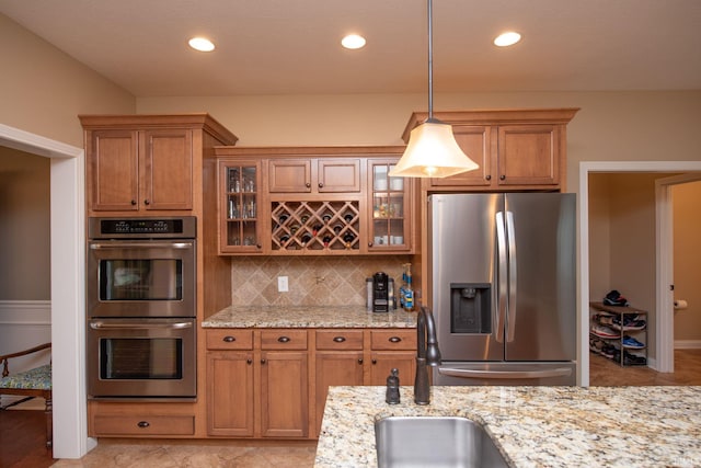 6118 Mackenzie Ct, West Lafayette, IN 47906 - kitchen with stainless steel appliances, a sink, brown cabinetry, light stone counters, and backsplash