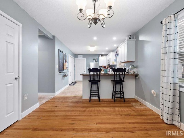 1346 Grayston Ave, Huntington, IN 46750 - kitchen featuring a chandelier, white cabinetry, a peninsula, light wood-type flooring, and a kitchen bar