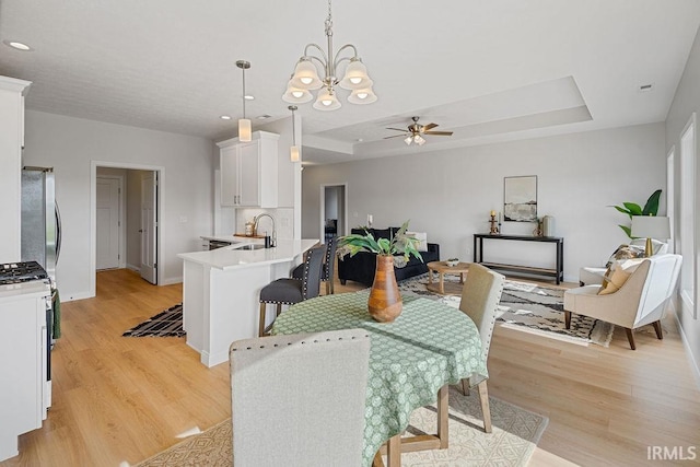 2487 Fiona Dr, Kokomo, IN 46902 - dining space featuring a chandelier, light wood-style flooring, a ceiling fan, a raised ceiling, and baseboards