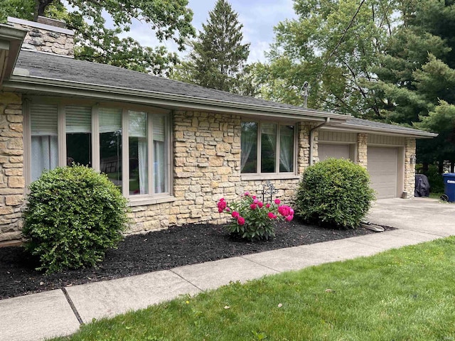 405 N Dogwood Ln, Muncie, IN 47304 - view of side of home with stone siding, an attached garage, driveway, a chimney, and a shingled roof