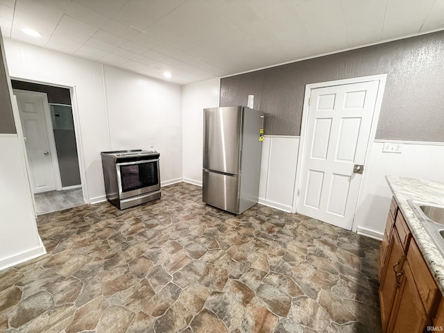 1226 N Union St, Kokomo, IN 46901 - kitchen with stainless steel appliances, stone finish flooring, light countertops, wainscoting, and brown cabinets