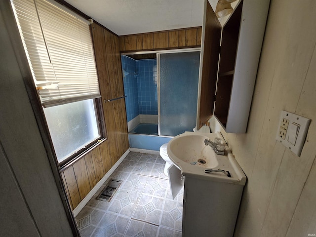 2710 W Virginia St, Evansville, IN 47712 - bathroom with wooden walls, tile patterned flooring, toilet, and combined bath / shower with glass door