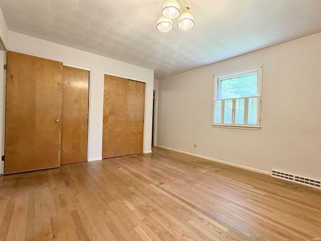 141 Indian Rock Dr, West Lafayette, IN 47906 - unfurnished bedroom with multiple closets, light wood-style floors, baseboards, baseboard heating, and a chandelier