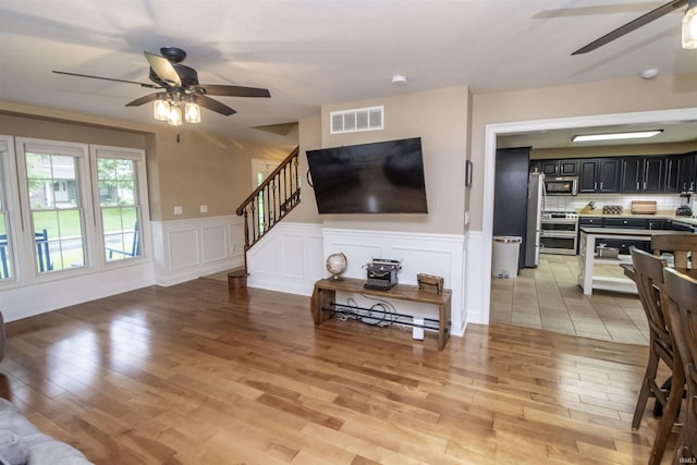 917 E Mill Creek Rd, Greensburg, IN 47240 - living room featuring a ceiling fan, light wood-style floors, stairway, and wainscoting