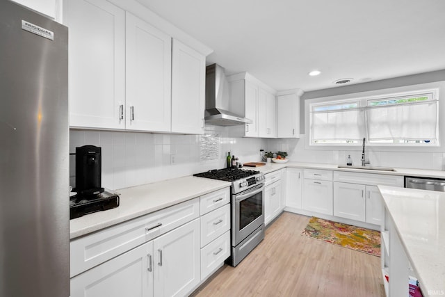 1718 Churchill Dr, South Bend, IN 46617 - kitchen featuring appliances with stainless steel finishes, wall chimney range hood, a sink, light wood finished floors, and white cabinetry