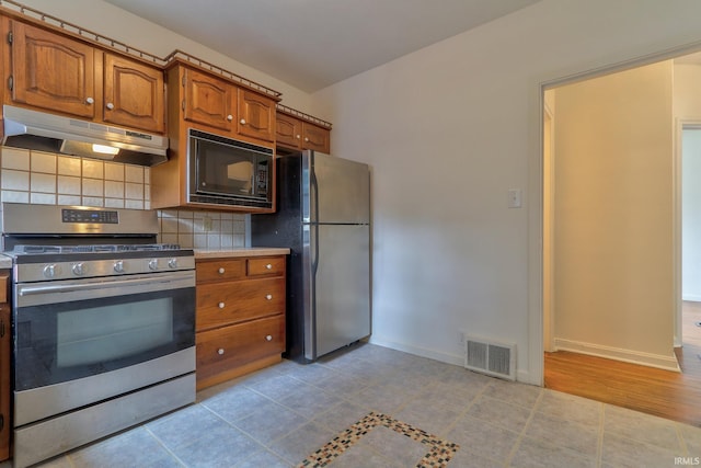 2305 E Virginia St, Evansville, IN 47711 - kitchen with stainless steel appliances, under cabinet range hood, brown cabinets, backsplash, and baseboards