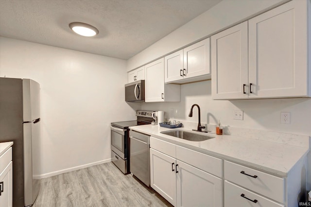 3220 E John Hinkle Pl Unit F, Bloomington, IN 47408 - kitchen featuring appliances with stainless steel finishes, a sink, white cabinets, light wood-style floors, and a textured ceiling