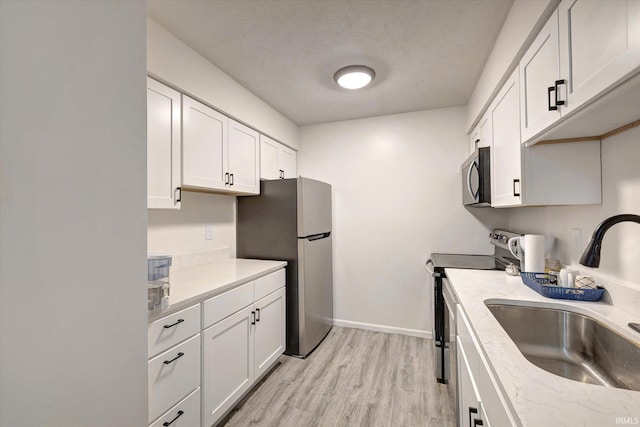 3220 E John Hinkle Pl Unit F, Bloomington, IN 47408 - kitchen with stainless steel appliances, a sink, light wood-style floors, white cabinetry, and light countertops