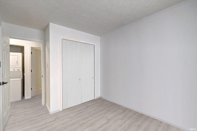 3220 E John Hinkle Pl Unit F, Bloomington, IN 47408 - unfurnished bedroom featuring stacked washer and clothes dryer, light wood finished floors, a closet, a textured ceiling, and baseboards