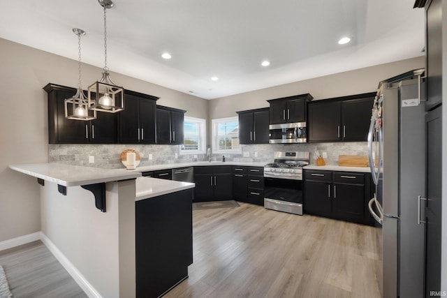 13909 Stone Table Blvd, Fort Wayne, IN 46845 - kitchen with appliances with stainless steel finishes, a peninsula, dark cabinets, tasteful backsplash, and light wood-type flooring