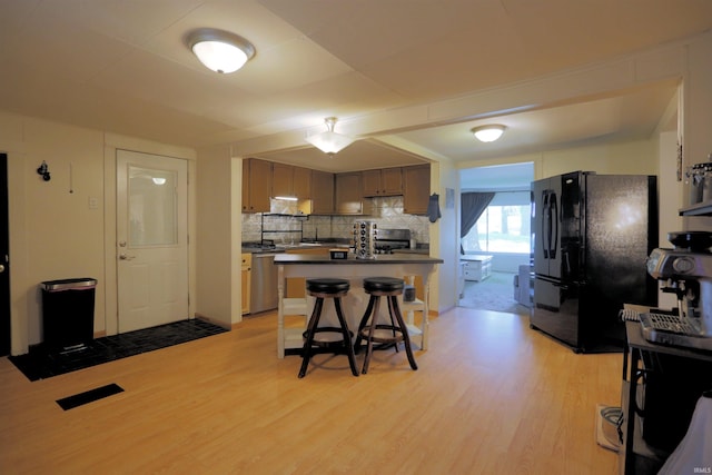 482 E Jefferson St, Andrews, IN 46702 - kitchen with freestanding refrigerator, light wood-style flooring, dark countertops, a kitchen bar, and decorative backsplash