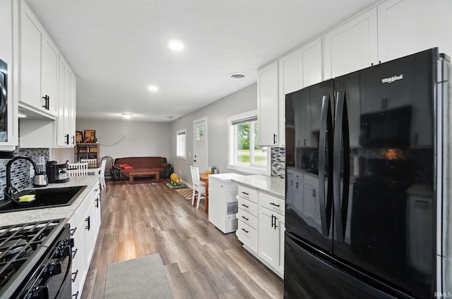 202 E Pickwick Dr, Syracuse, IN 46567 - kitchen with black appliances, a sink, decorative backsplash, open floor plan, and white cabinetry