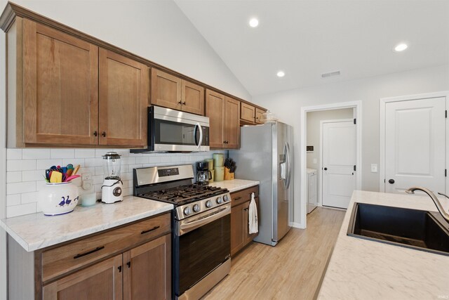 3436 Fawn Creek Blvd, Waterloo, IN 46793 - kitchen with appliances with stainless steel finishes, a sink, decorative backsplash, lofted ceiling, and light wood finished floors