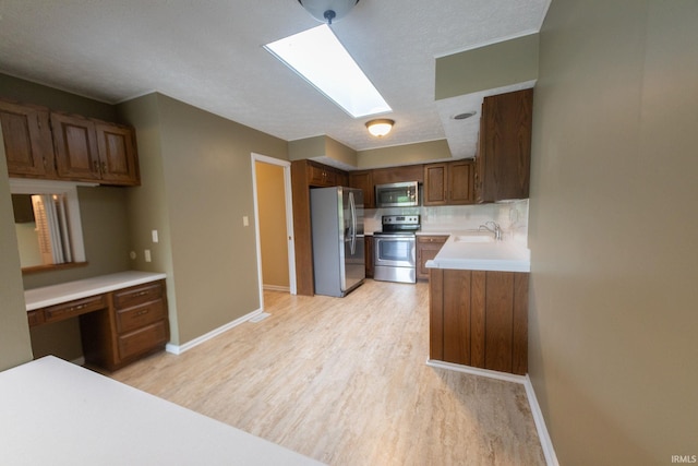 604 W Soutar Dr, Bloomington, IN 47403 - kitchen with appliances with stainless steel finishes, a skylight, light wood-style flooring, a sink, and baseboards