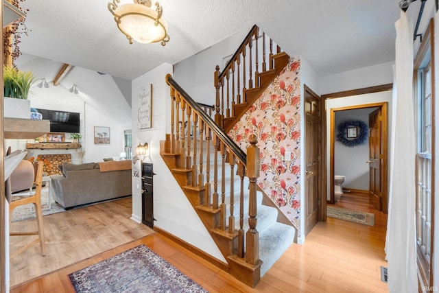 15025 Water Oak Pl, Huntertown, IN 46748 - staircase featuring wood finished floors, a fireplace, a textured ceiling, vaulted ceiling, and baseboards