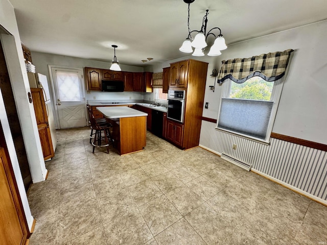 2940 19th St, Columbus, IN 47201 - kitchen with black appliances, a kitchen island, light countertops, wainscoting, and a chandelier