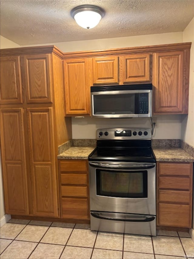 999 Inderrieden Rd, Chandler, IN 47610 - kitchen with appliances with stainless steel finishes, a textured ceiling, brown cabinetry, light tile patterned floors, and dark countertops