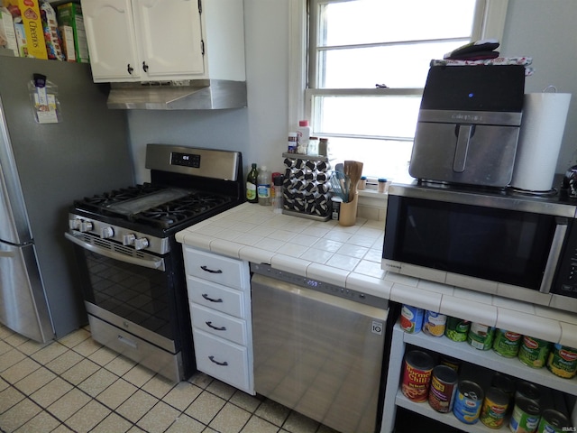 1612 N Wellington St, South Bend, IN 46628 - kitchen with appliances with stainless steel finishes, range hood, tile countertops, white cabinets, and light tile patterned flooring