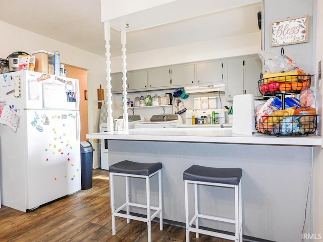2363 N Oak Dr, Bluffton, IN 46714 - kitchen featuring freestanding refrigerator, washing machine and clothes dryer, dark wood-type flooring, a breakfast bar area, and a peninsula