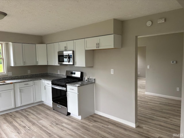 724 Iroquois Dr, Anderson, IN 46012 - kitchen featuring appliances with stainless steel finishes, light wood-style floors, a textured ceiling, baseboards, and white cabinets