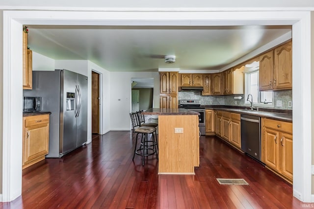 7782 S Warren Rd, Warren, IN 46792 - kitchen featuring stainless steel appliances, a sink, dark countertops, dark wood-style floors, and a breakfast bar area