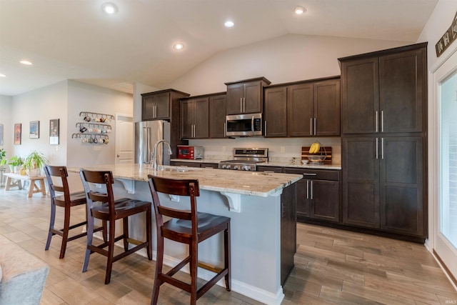 7937 Boydon Ct, Evansville, IN 47715 - kitchen featuring appliances with stainless steel finishes, a center island with sink, vaulted ceiling, dark brown cabinets, and a kitchen bar