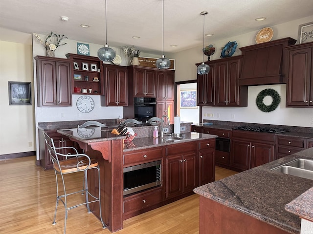 5533 N 150 Rd E, Urbana, IN 46990 - kitchen featuring black appliances, a sink, a center island with sink, light wood-type flooring, and a breakfast bar