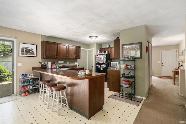 17411 Woodhurst Rd, Granger, IN 46530 - kitchen featuring freestanding refrigerator, white microwave, a sink, a peninsula, and a kitchen bar
