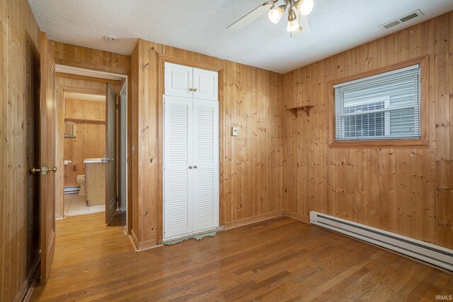 8056 E N Rd, Syracuse, IN 46567 - unfurnished bedroom featuring a baseboard heating unit, wood finished floors, a closet, wood walls, and ceiling fan