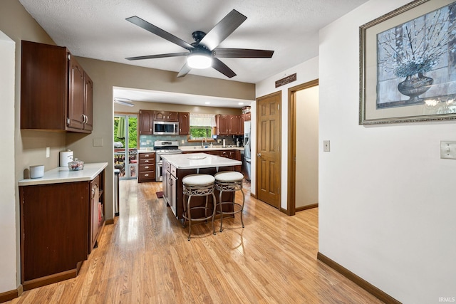 30986 Creekwood Ter, Osceola, IN 46561 - kitchen with appliances with stainless steel finishes, light wood finished floors, a ceiling fan, and a kitchen breakfast bar