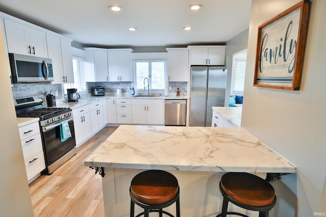 5547 N W Shafer Dr, Monticello, IN 47960 - kitchen featuring appliances with stainless steel finishes, a sink, a kitchen breakfast bar, tasteful backsplash, and light wood-style flooring