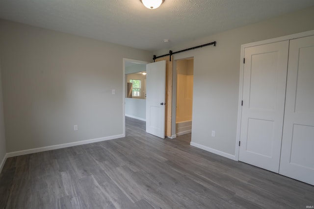 1109 E 6th St, Fowler, IN 47944 - unfurnished bedroom featuring a barn door, wood finished floors, baseboards, a closet, and a textured ceiling