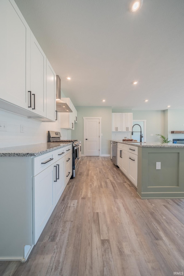 848 W S St, Upland, IN 46989 - kitchen featuring stainless steel appliances, wall chimney range hood, a sink, white cabinetry, and light wood-style floors